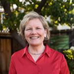 A middle-aged woman with blonde hair and a red shirt smiling at the camera